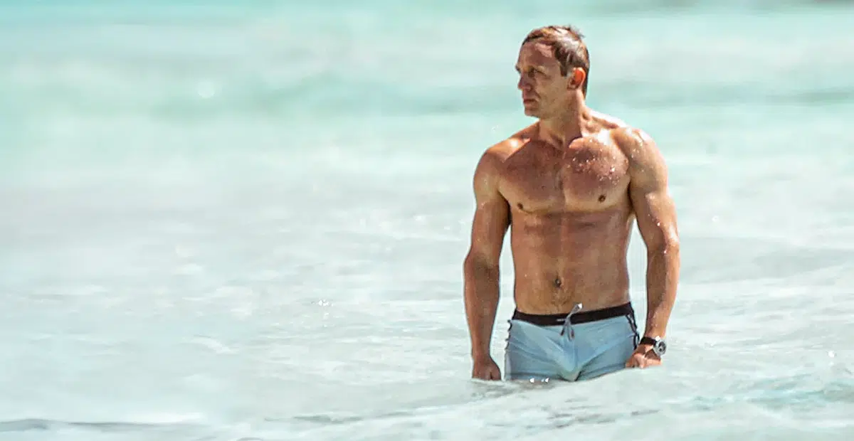 Daniel craig sortant de l'eau sur une plage, représentant le physique de James Bond, torse nu et en short de bain.
