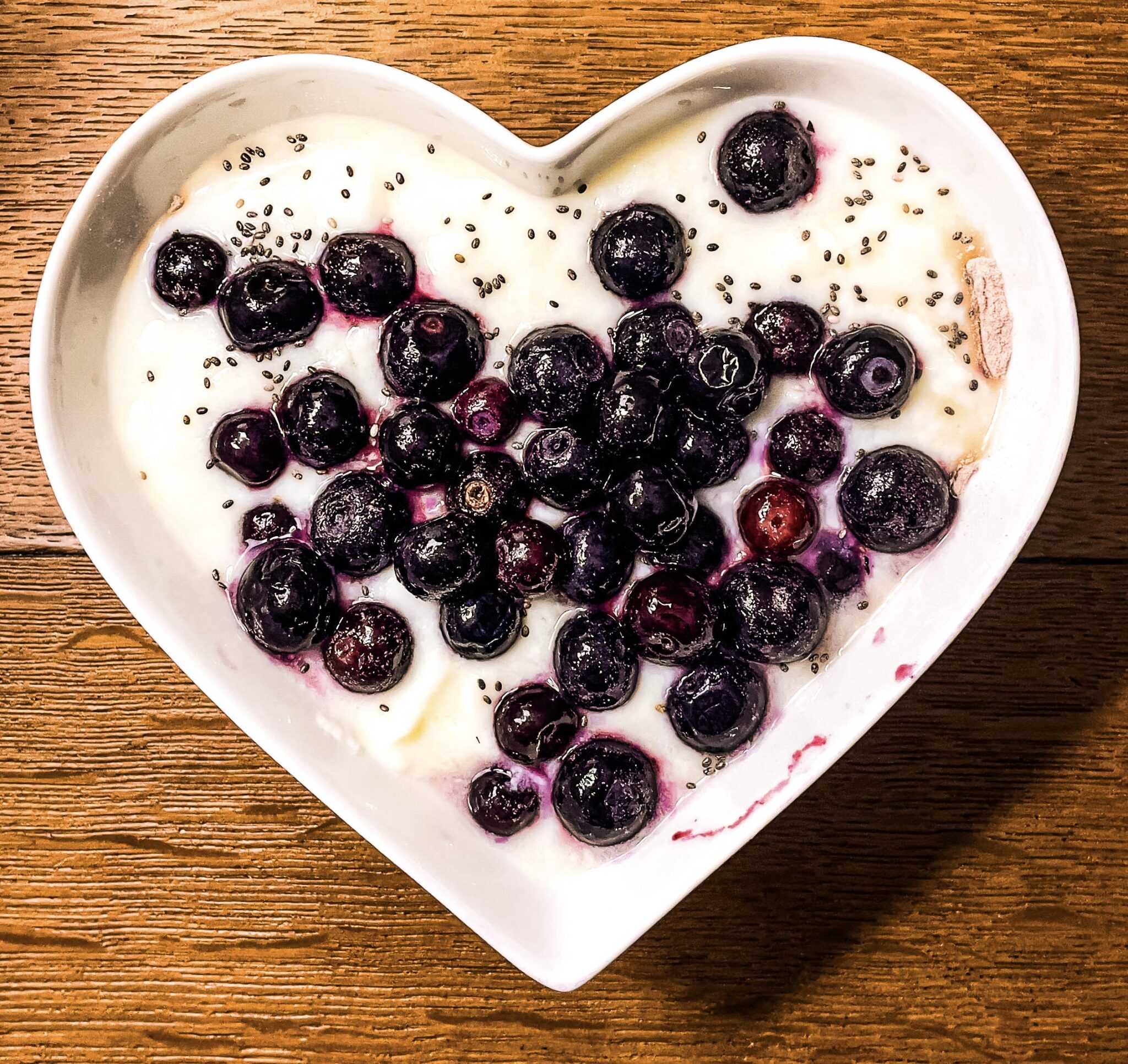 Bol en forme de cœur rempli de yaourt protéiné, myrtilles et graines de chia, parfait pour un petit-déjeuner sain et riche en protéines.