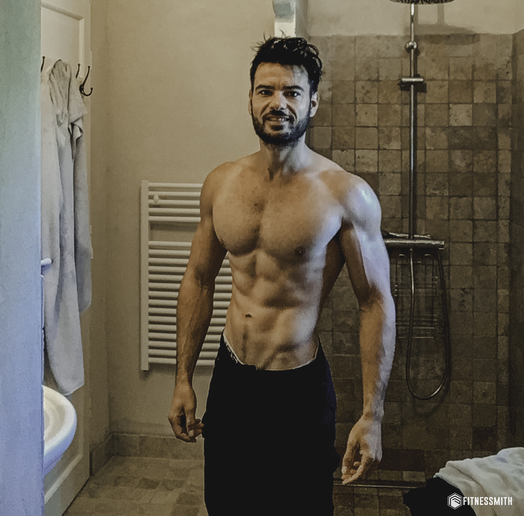 Homme torse nu debout dans une salle de bain, montrant des abdominaux visibles au repos grâce à un entraînement régulier et une faible masse grasse