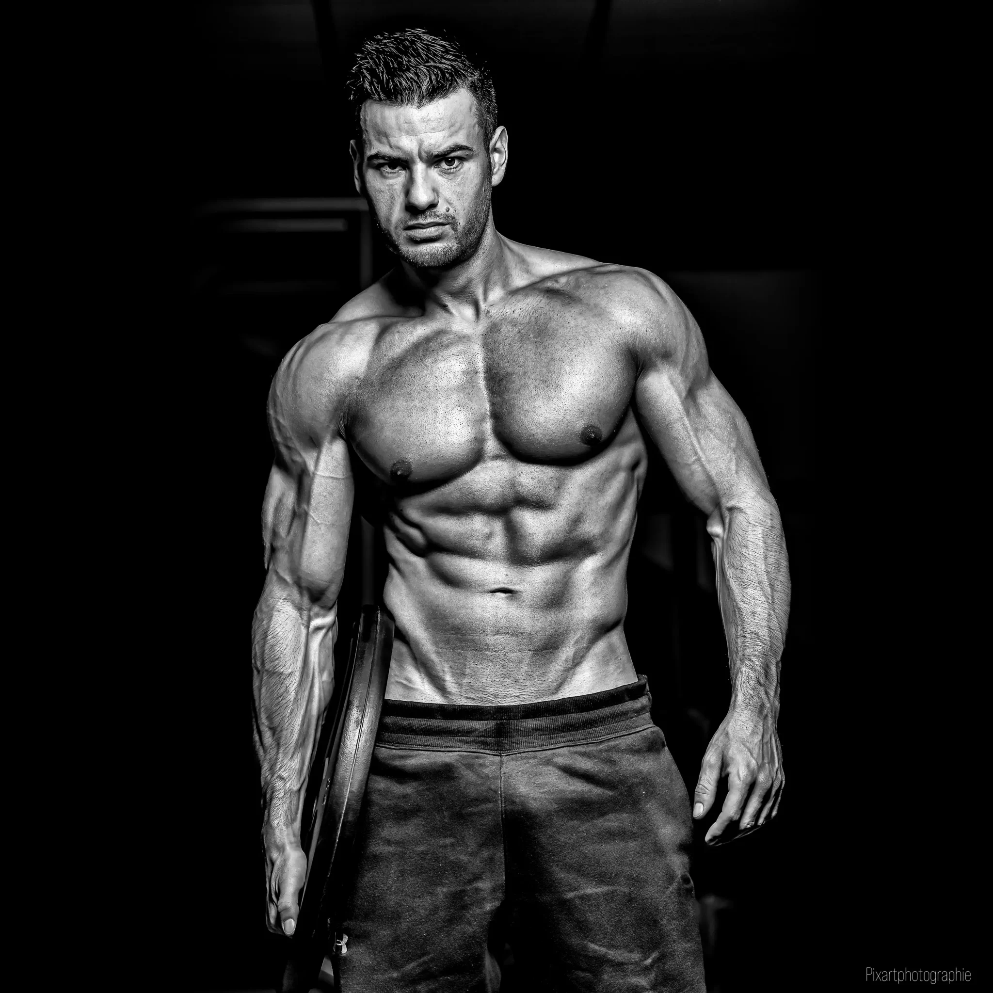 homme musclé sec en salle de sport tenant une plaque de musculation, représentant un physique sculpté obtenu grâce au programme sèche musculation Fitnessmith