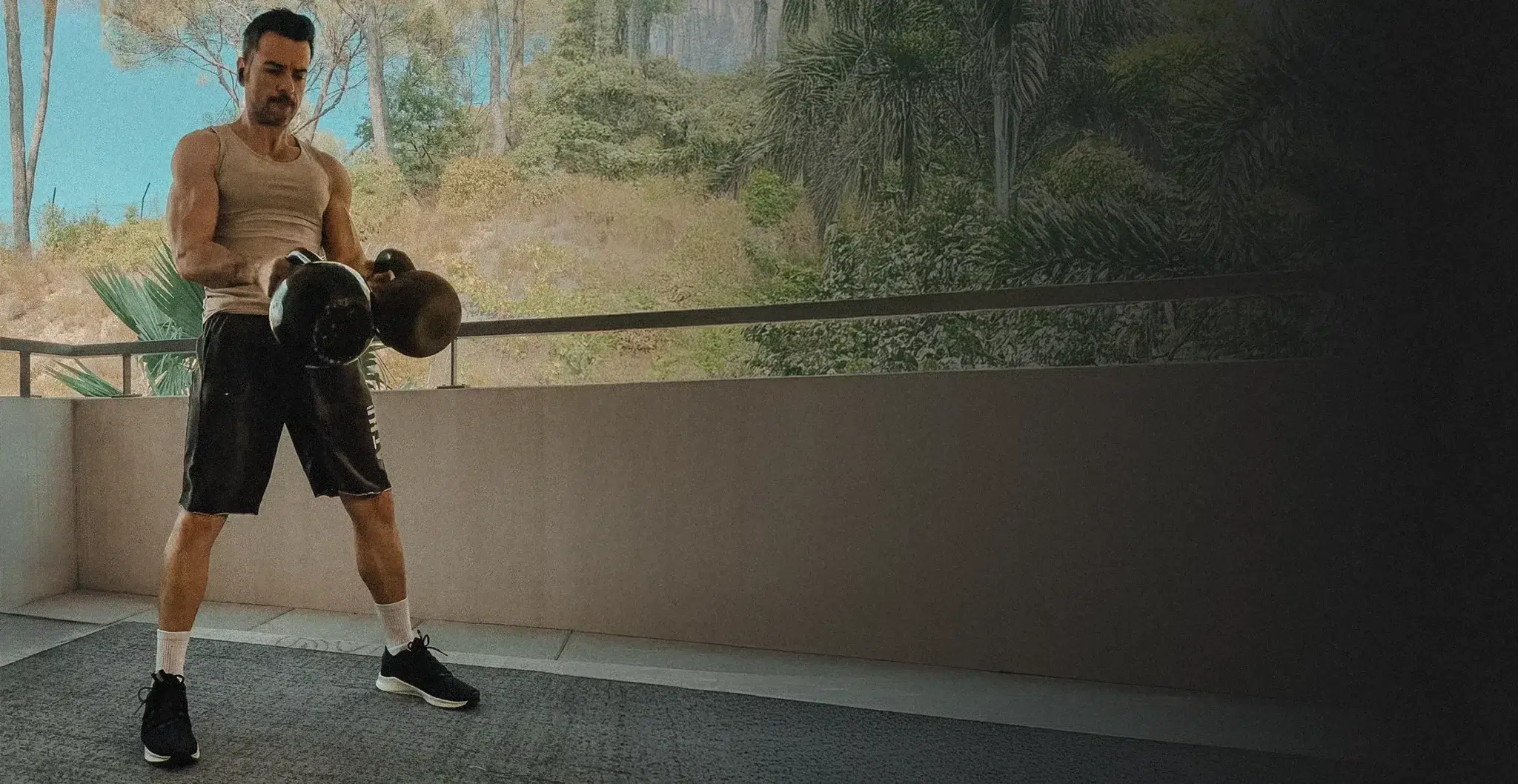 Homme musclé réalisant un double swing avec kettlebells sur balcon, entraînement EMOM en extérieur