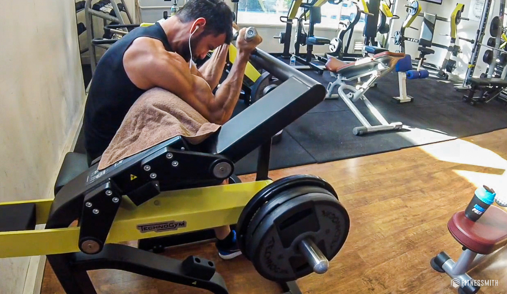 Athlète effectuant un curl biceps à la machine en salle de sport, illustrant l'effort musculaire et la gestion des douleurs.