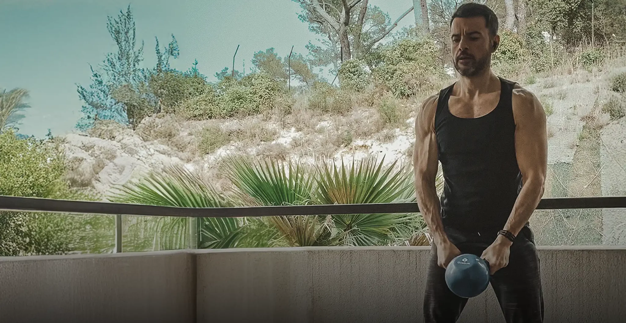 Homme musclé s'entraînant avec kettlebell sur son balcon en écoutant de la musique, exemple d'efficacité maximale pendant l'entraînement.